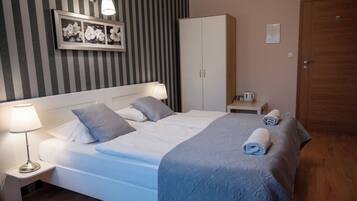 A neatly made bed with pillows, a bedside lamp, a framed picture on the wall, a wardrobe, and a door.