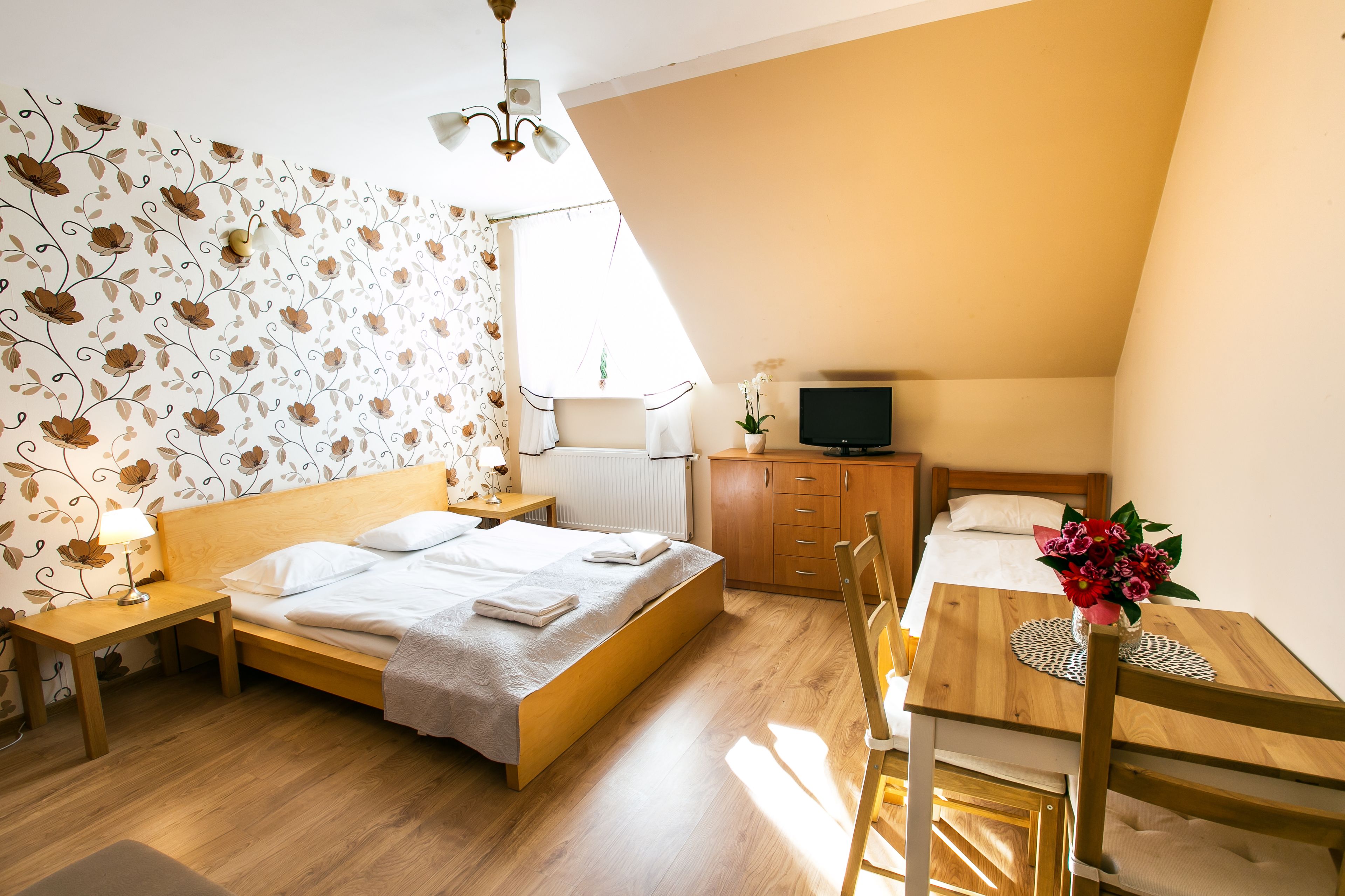 Un dormitorio con cama de madera, mesita de noche, lámpara, televisor y una pequeña mesa con flores.