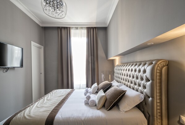 A modern hotel room with a large bed, a flat-screen TV, and a chandelier. - Lea Luxury Rooms (Rome)