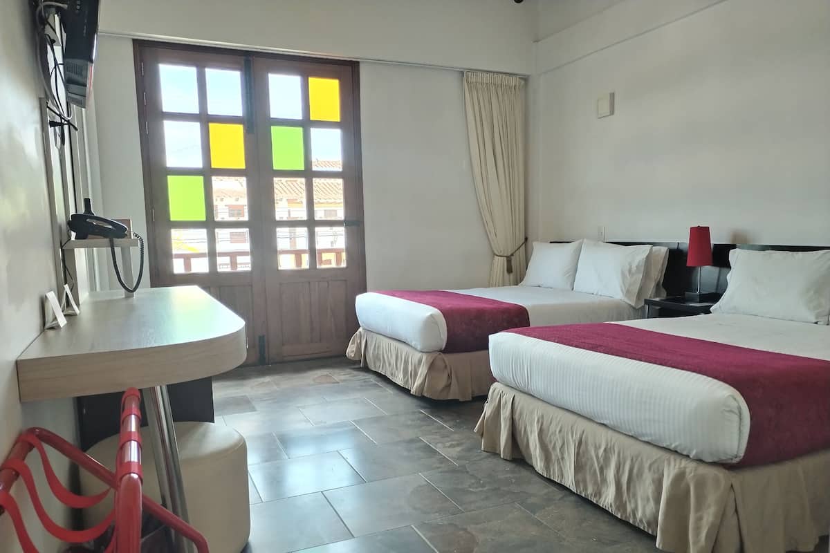 Habitación de hotel con dos camas, un escritorio, una silla, un teléfono y una ventana con cortinas.
