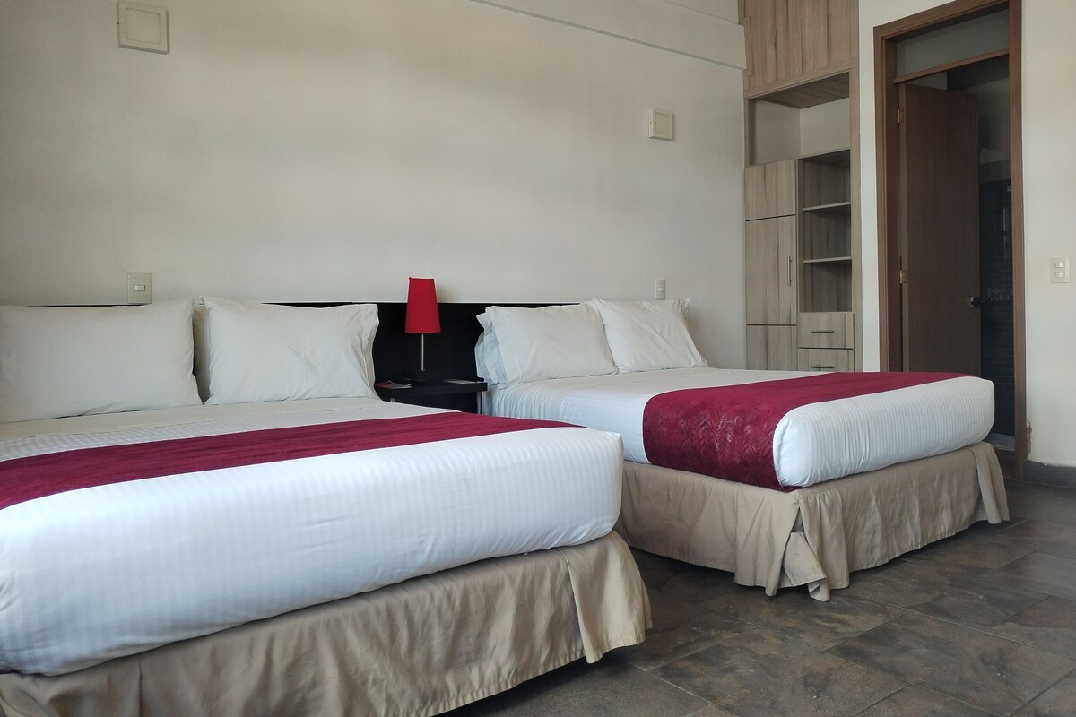 A hotel room with two beds, a red lamp, a wardrobe, and a door leading to a bathroom.