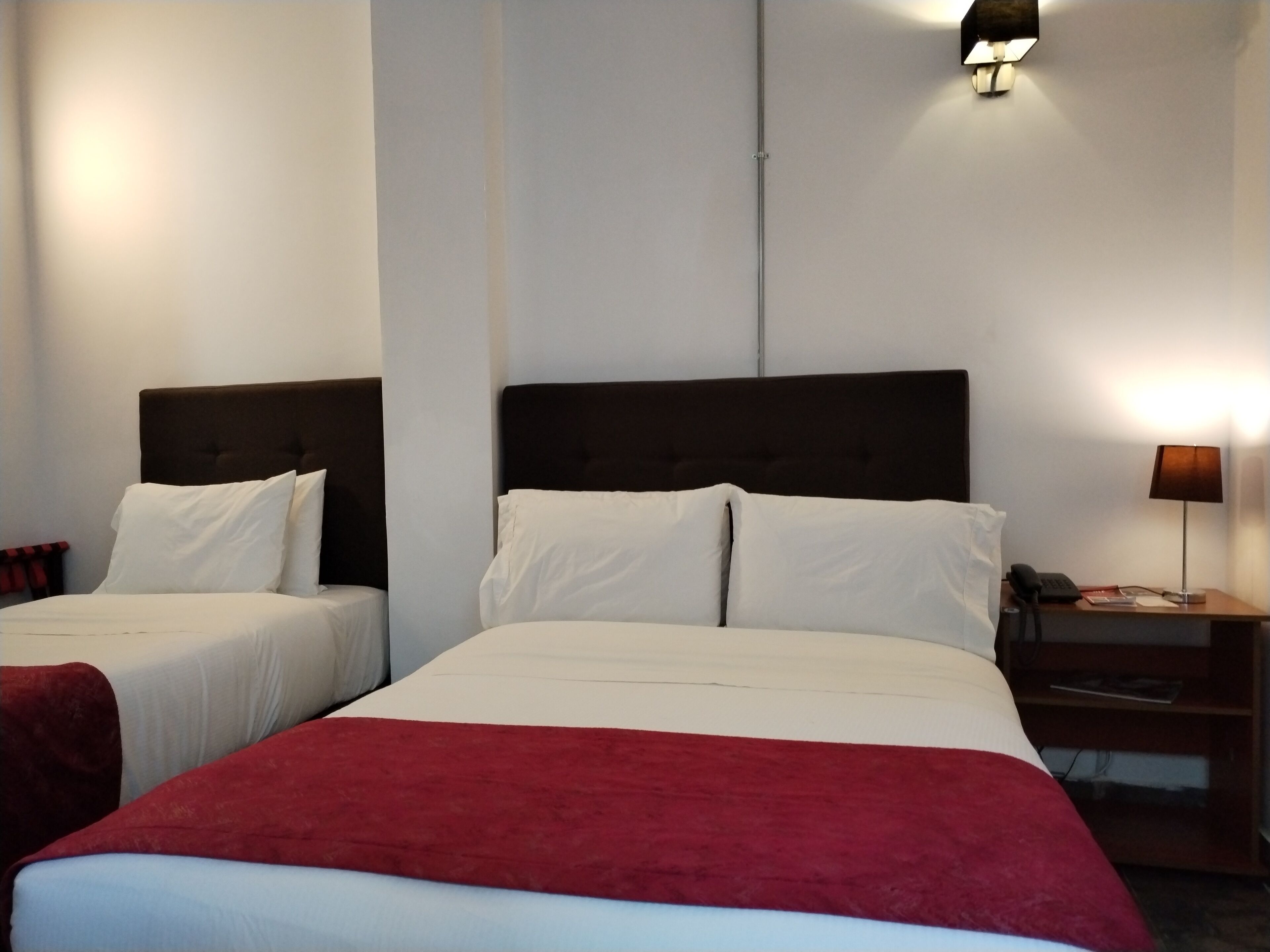 Habitación de hotel con dos camas, cada una con ropa blanca de cama y una colcha roja. Hay una mesita de noche con una lámpara y un teléfono.