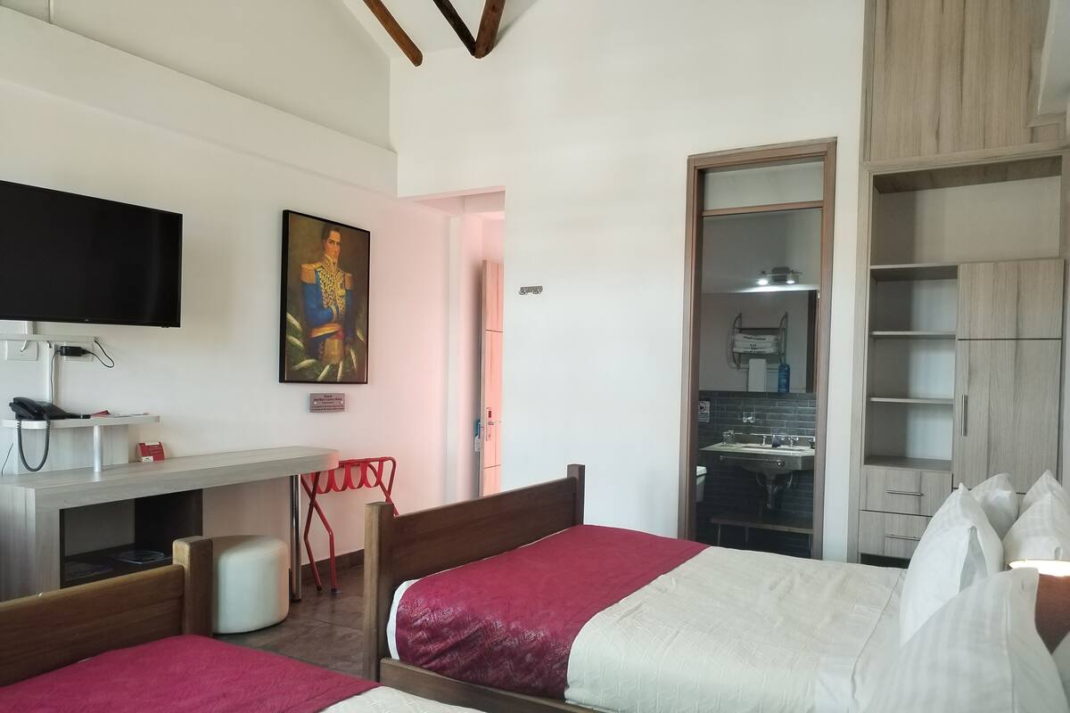 Una habitación de hotel con dos camas, un escritorio con teléfono, una televisión y un cuadro en la pared.