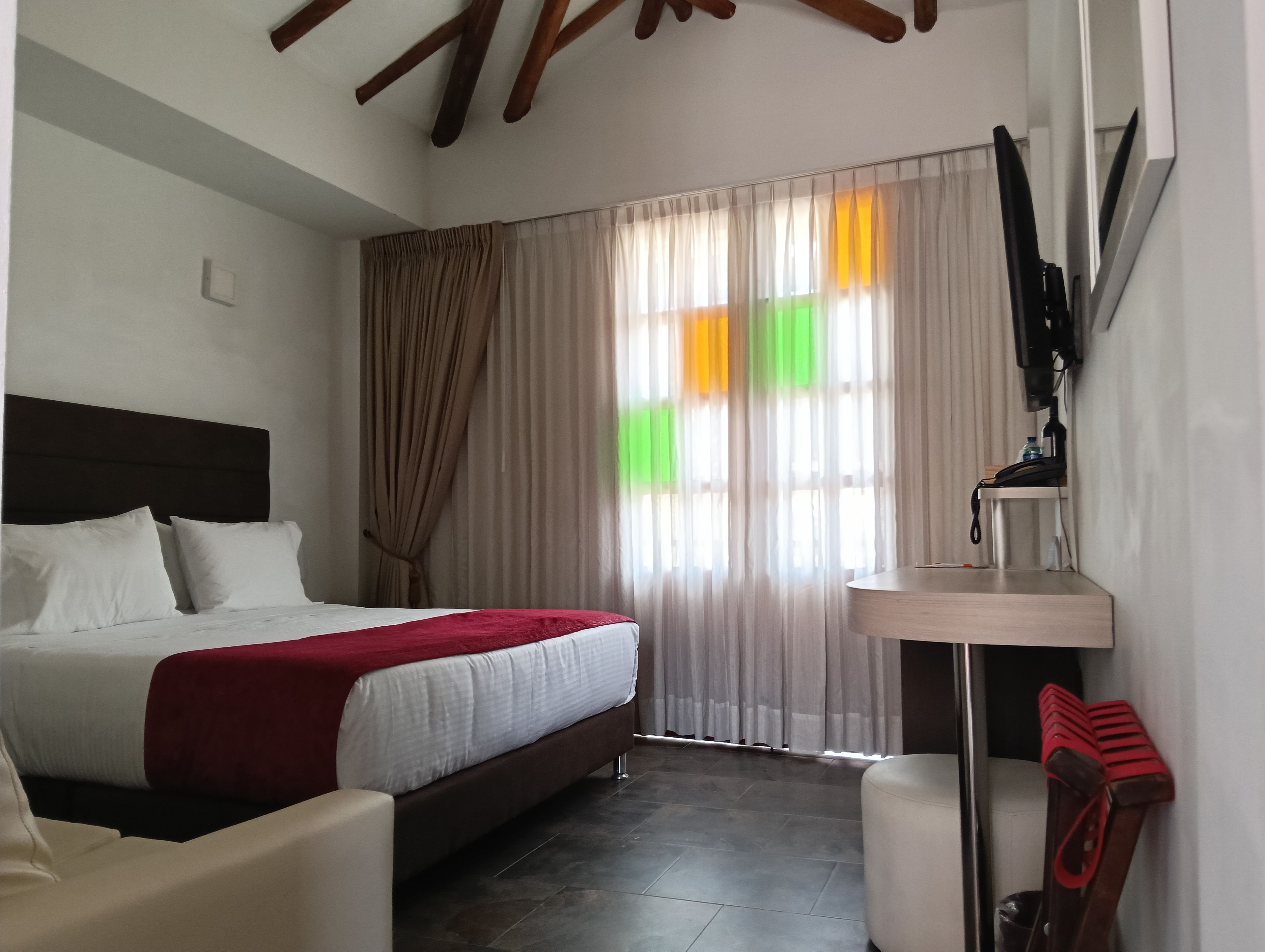 Une chambre d’hôtel équipée d’un lit, d’une chaise, d’un bureau avec un téléphone et d’un téléviseur fixé au mur.