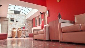 A spacious room with a red wall, a skylight, a sofa, a table with vases, and a patterned floor. - Hotel Capitán Ricaurte (Villa de Leyva)