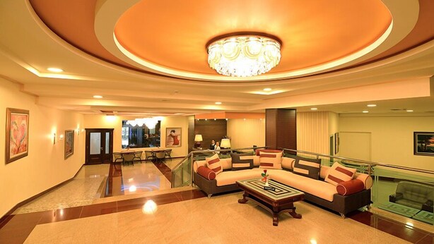 A spacious lobby with a curved ceiling, a large chandelier, a seating area with sofas and a coffee table, and a glass railing overlooking the lobby. - Hotel Austria (Tirana)
