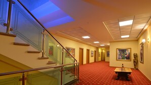A hotel hallway with a red carpet, a staircase with glass railings, and artwork on the walls. - Hotel Austria (Tirana)
