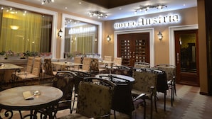A hotel lobby with round tables and chairs, large windows with curtains, and a sign that reads "HOTEL Austria". - Hotel Austria (Tirana)