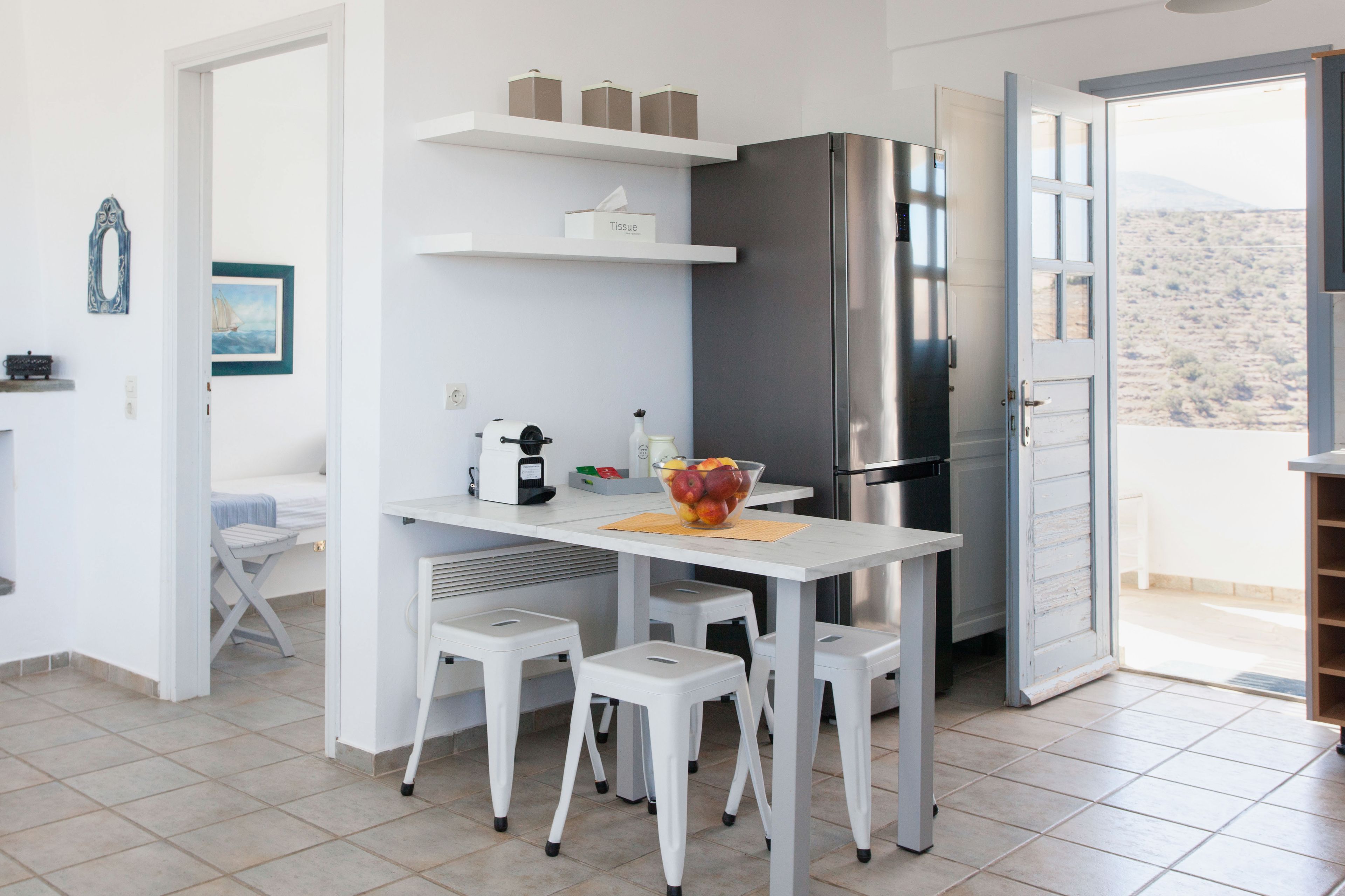 Une cuisine moderne dotée d’un réfrigérateur en acier inoxydable, de meubles blancs et d’un coin repas avec une table et des tabourets.