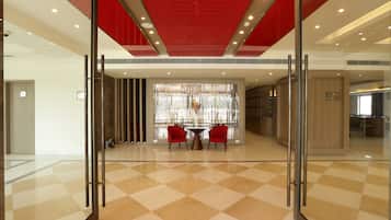 Vestíbulo de hotel con piso a cuadros, techo rojo y separador de vidrio con una mesa y sillas.
