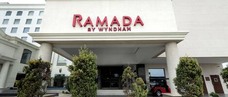 The exterior of the Ramada by Wyndham hotel with a prominent entrance, columns, and a red vehicle parked in front.