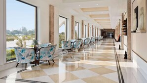 A hotel corridor with a checkered floor, large windows, and rows of chairs. - Ramada by Wyndham Lucknow Hotel and Convention Center (Lucknow)