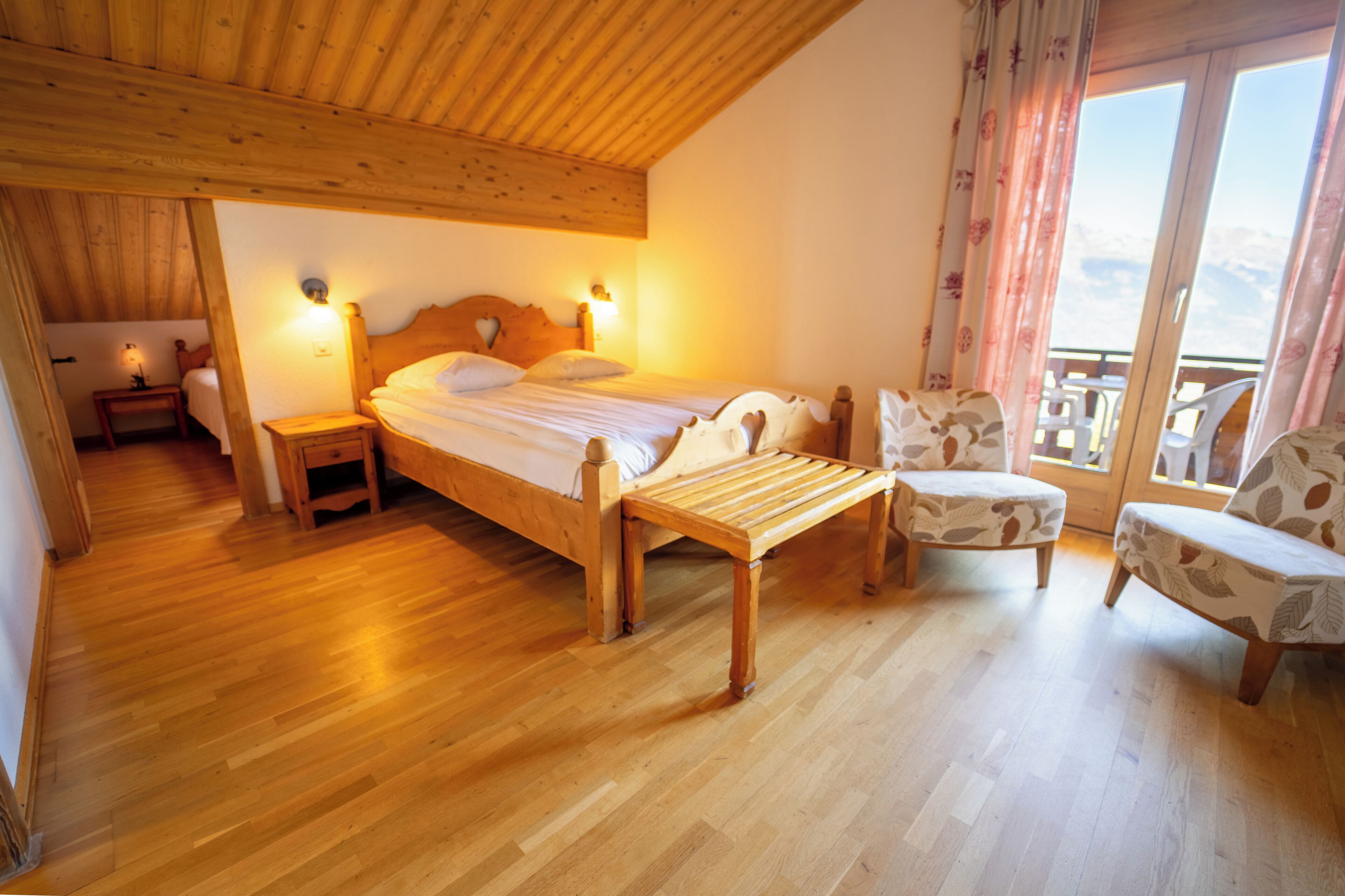 Un dormitorio con suelo de madera, una cama, mesitas de noche y una silla.