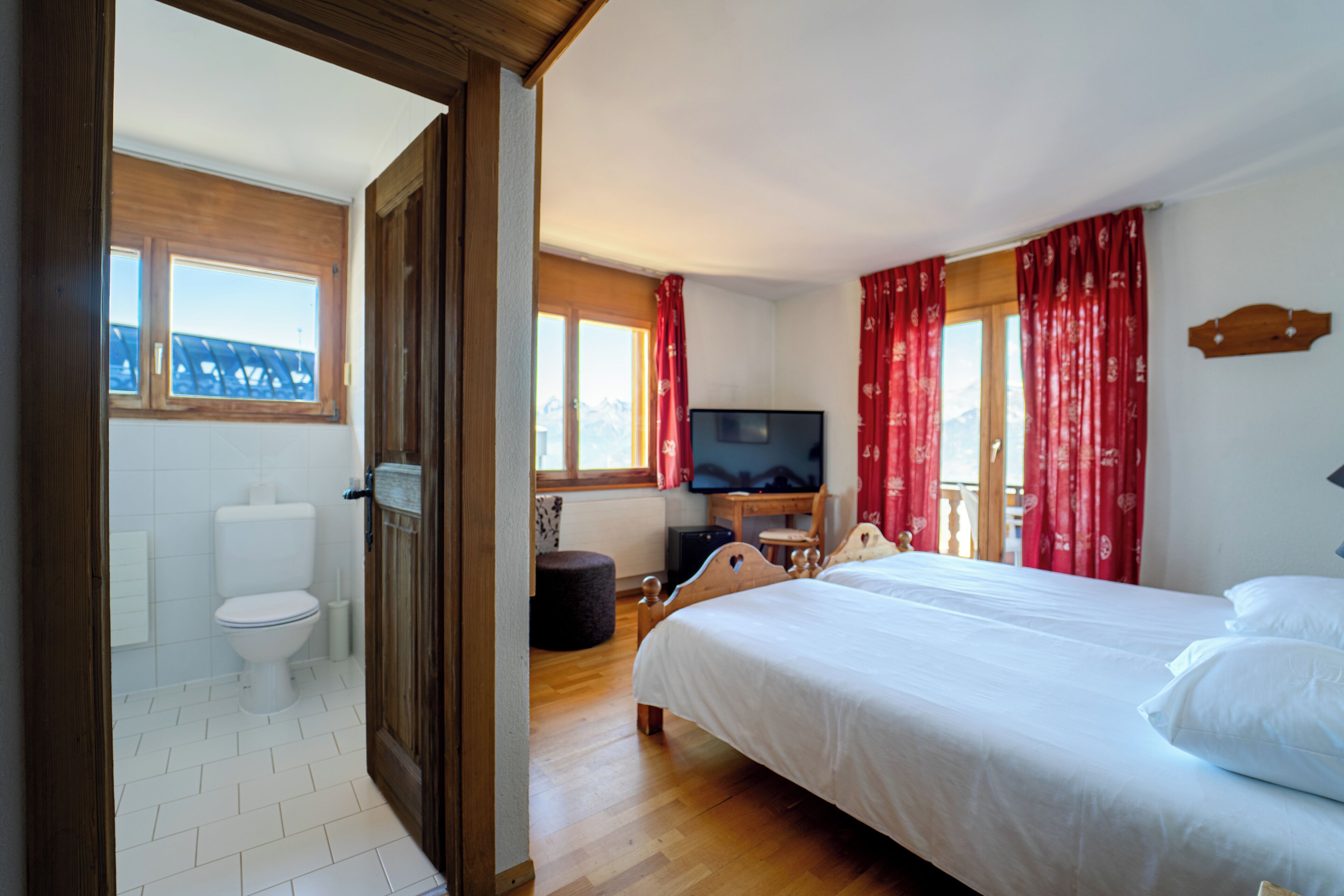 A bedroom with a bed, a television, and a bathroom with a toilet and sink.