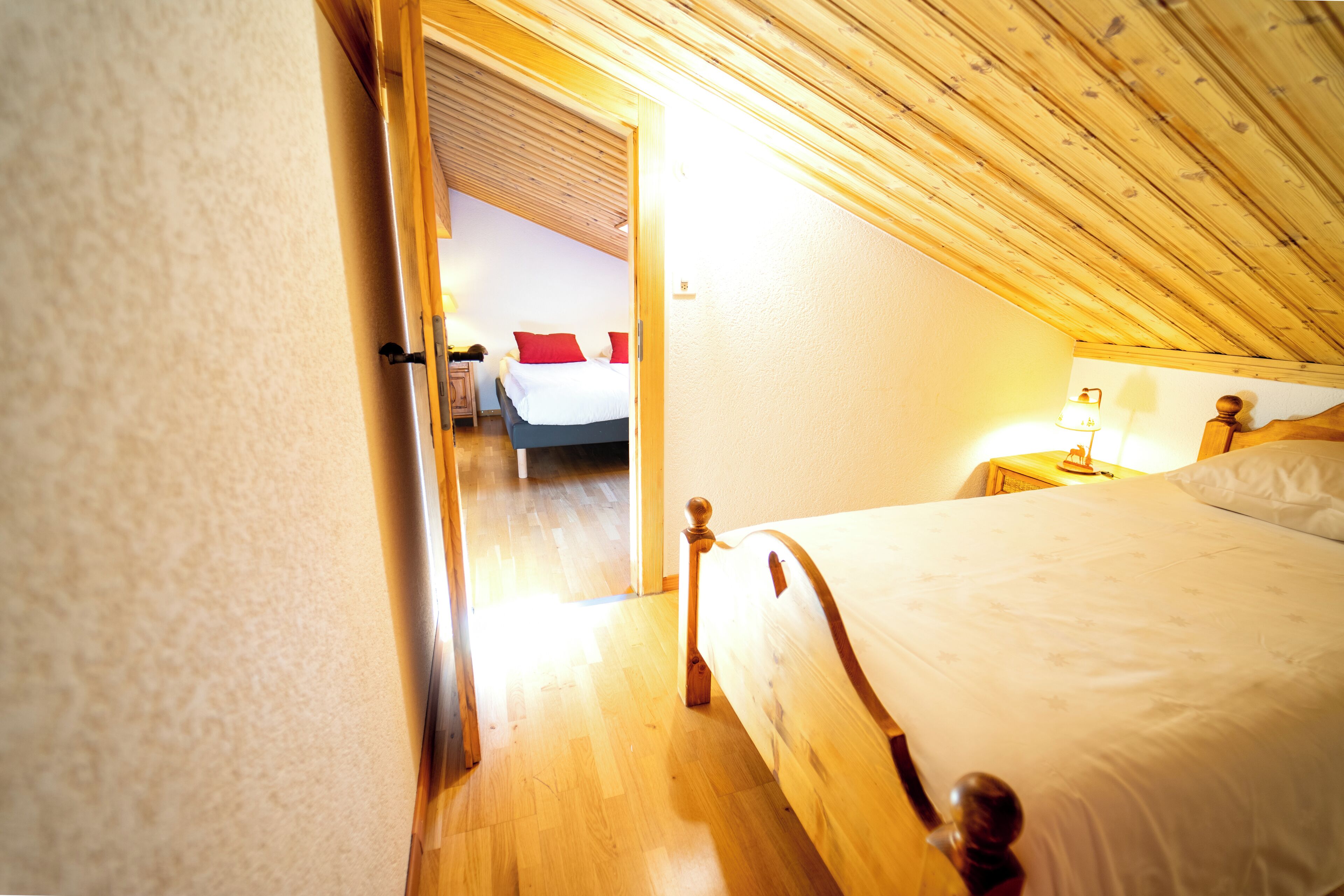 A bedroom with a wooden ceiling, a bed with a white bedspread, and a nightstand with a lamp.