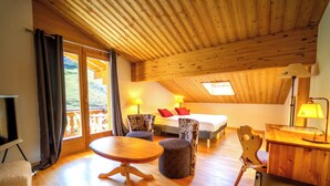 Een knus vertrek met houten plafond, een bed met rode kussens, een bureau met lamp en uitzicht op een balkon.