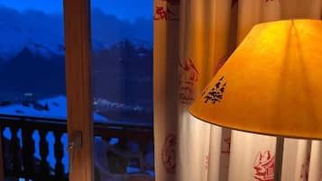 Une pièce avec vue sur des montagnes enneigées, visible à travers une fenêtre, des rideaux aux motifs traditionnels et une lampe.