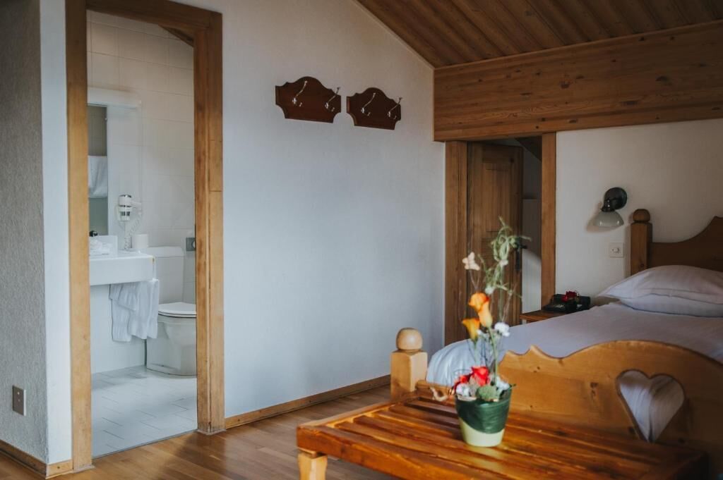A bedroom with a wooden headboard, a bedside table with a vase of flowers, and a view into the bathroom.