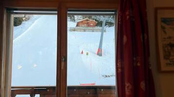 Una habitación con vista a un paisaje nevado a través de una ventana, una puerta de madera y una cortina.