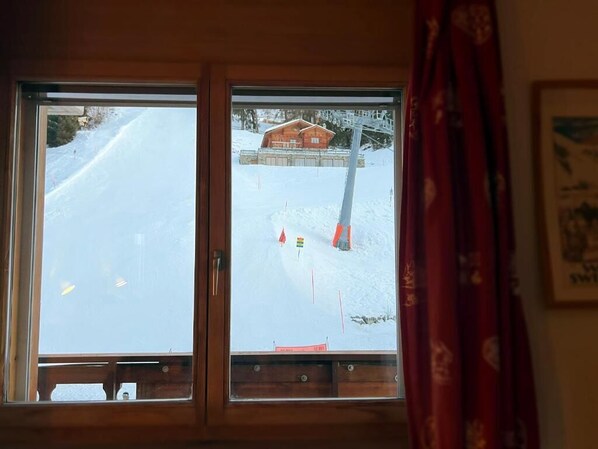 Una habitación con vista a un paisaje nevado a través de una ventana, una puerta de madera y una cortina.