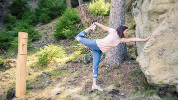 A person performing a yoga pose outdoors, with a wooden post and a large rock nearby.