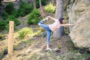 A person performing a yoga pose outdoors, with a wooden post and a large rock nearby.