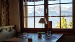 Een kamer met een tafel en een raam dat uitkijkt op een bergachtig landschap.
