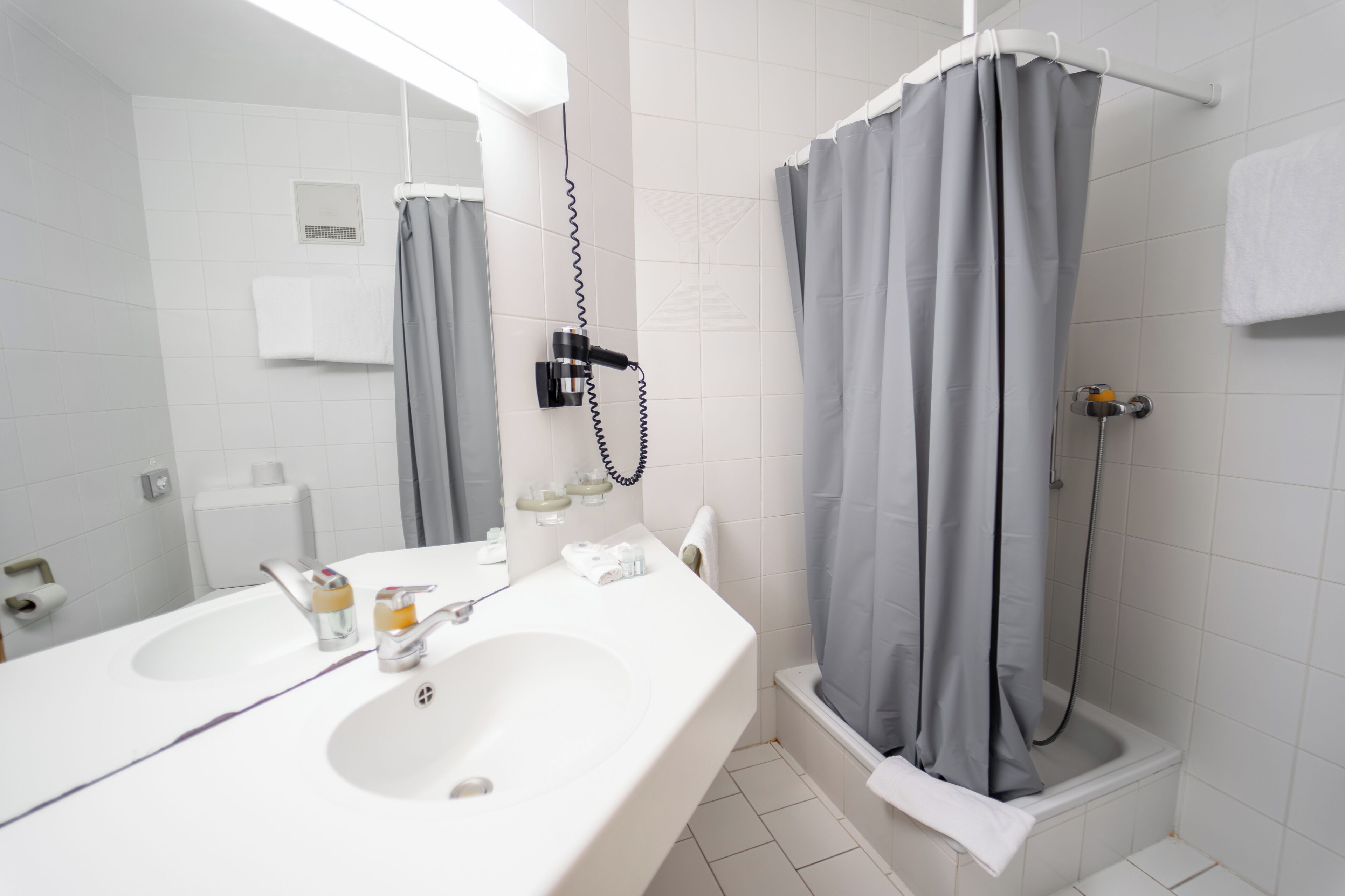 Un baño con lavamanos doble, un espejo, una ducha con cortina gris y un perchero para toallas.