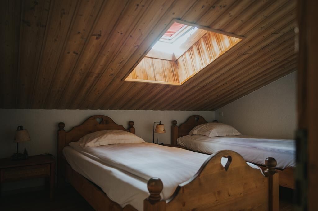 Quarto com duas camas de madeira, um claraboia e uma mesa de cabeceira com abajur.