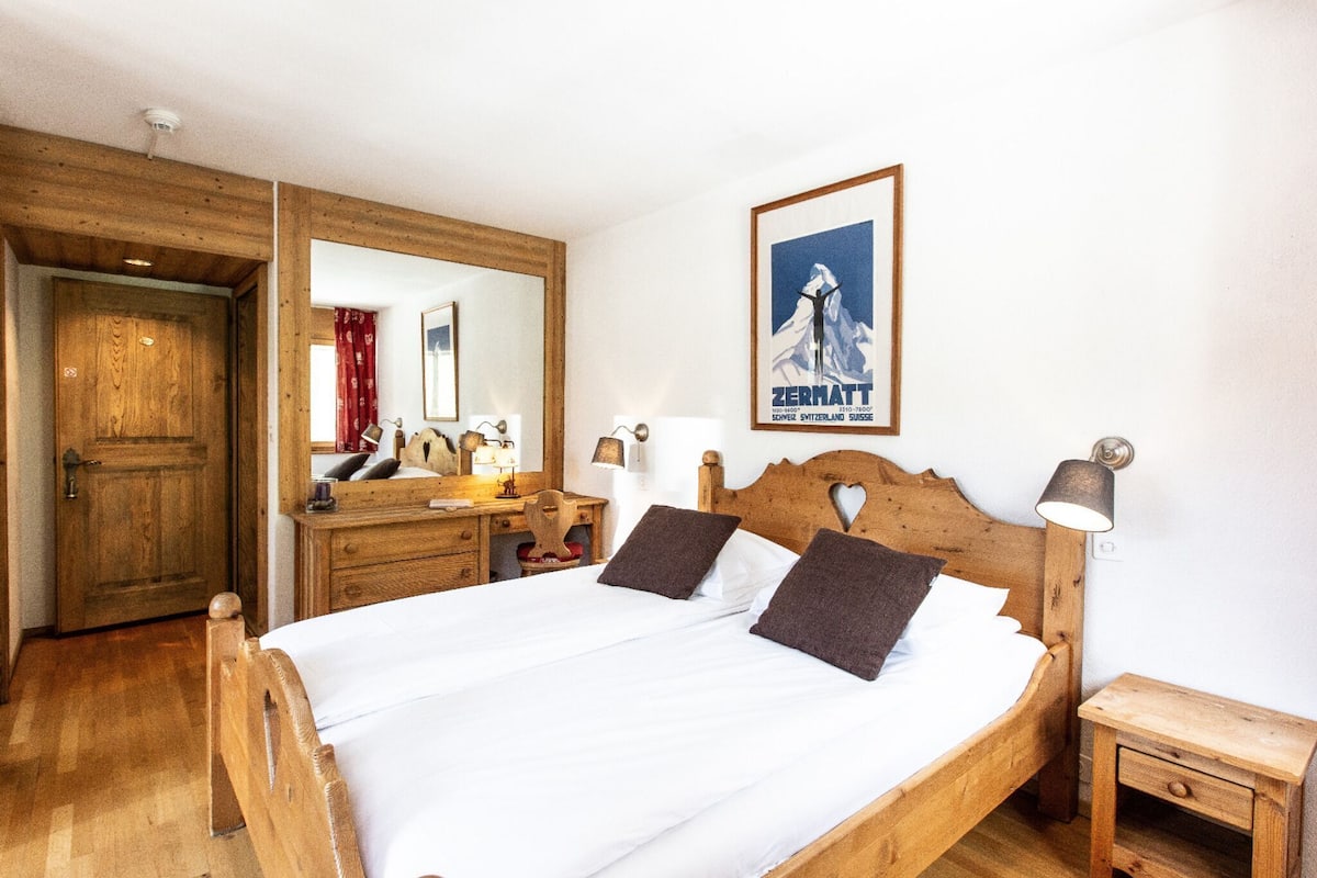 A wooden bed with two pillows, a wooden nightstand, a dresser, a mirror, and a framed picture on the wall.