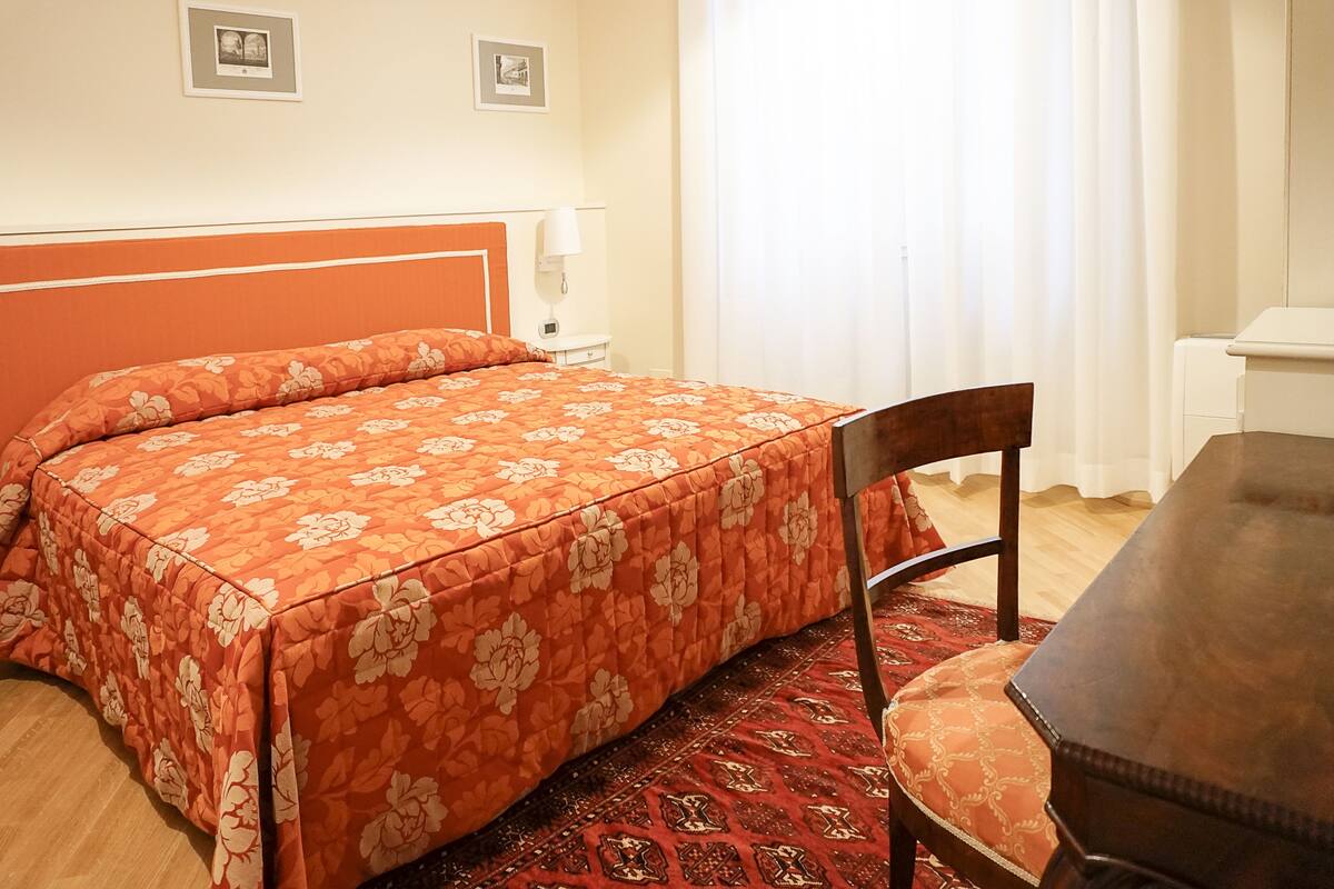 Une chambre d’hôtel avec un lit, une chaise, une table et une fenêtre avec des rideaux.