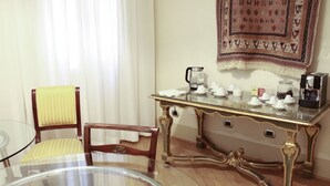 Una habitación con una mesa de vidrio, una silla de madera con cojín amarillo, una mesita con cafetera, tazas y un tapete decorativo.