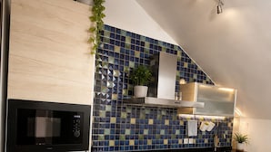 A modern kitchen with a built-in microwave, oven, and washing machine, a tiled backsplash, and wooden cabinets. - Ático Centro Málaga (Málaga)
