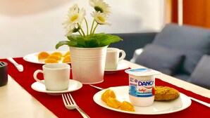 A breakfast setting with a red tablecloth, a white coffee cup, a white mug, a white plate with a cookie, a white cup with a plant, and a white plate with orange slices. - Ático Centro Málaga (Málaga)