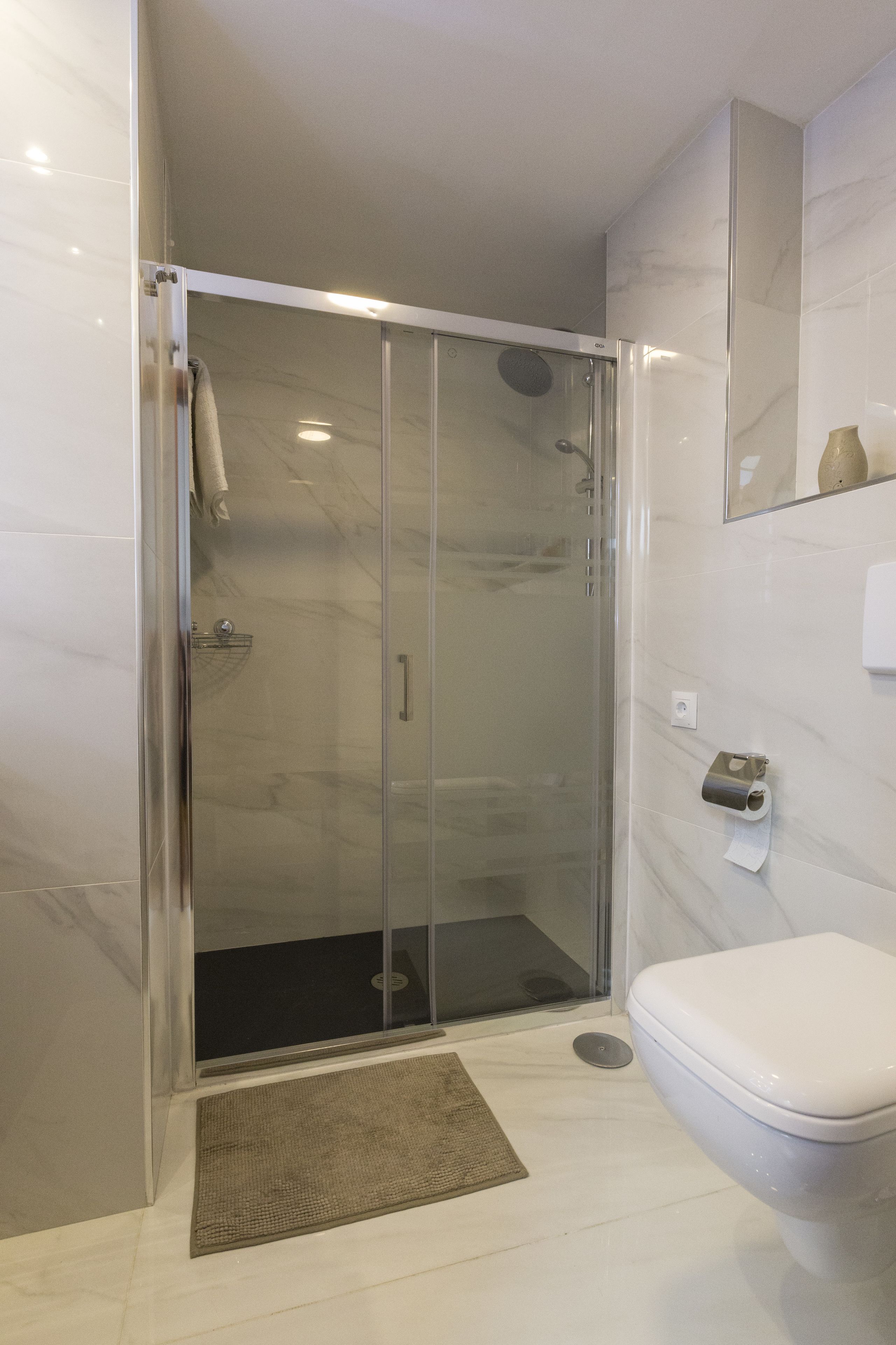 A modern bathroom with a glass-enclosed shower, a toilet, and a marble-tiled wall.