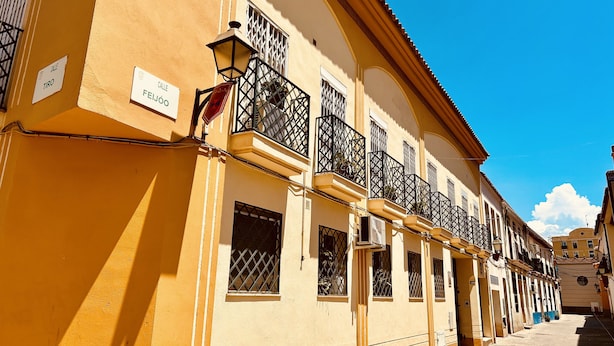 A yellow building with multiple windows and balconies, a street in front, and a clear blue sky. - Ático Centro Málaga (Málaga)