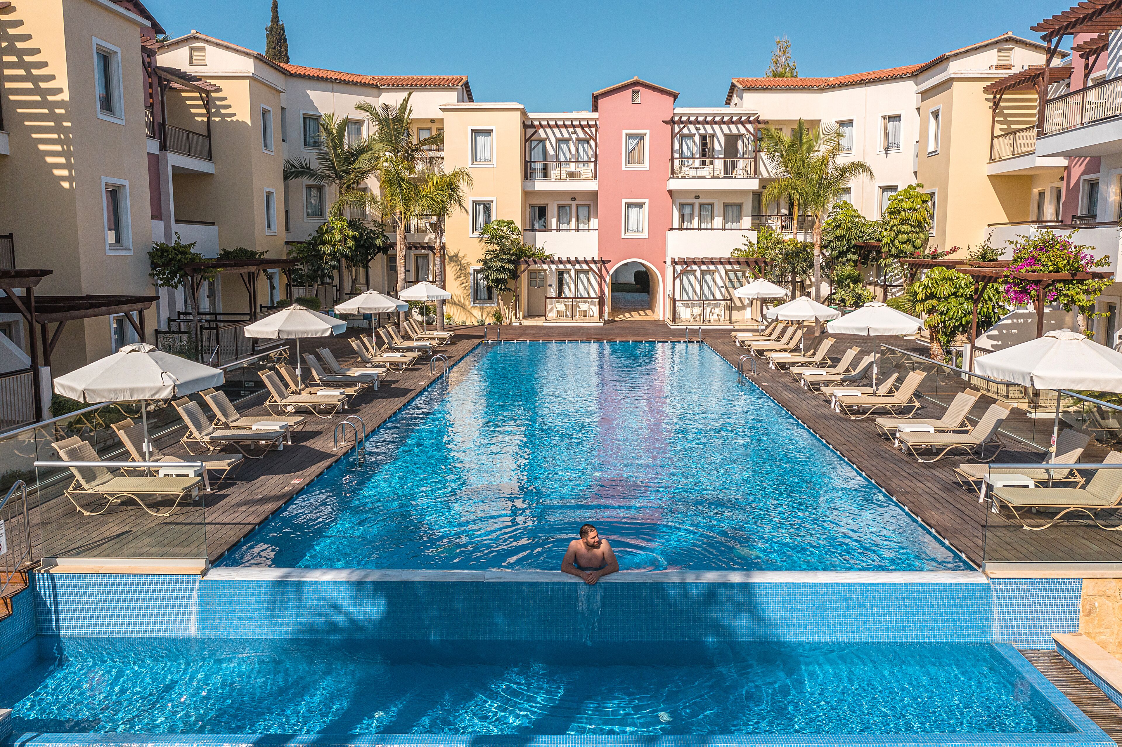 A swimming pool with lounge chairs and umbrellas, surrounded by multi-story buildings with balconies.