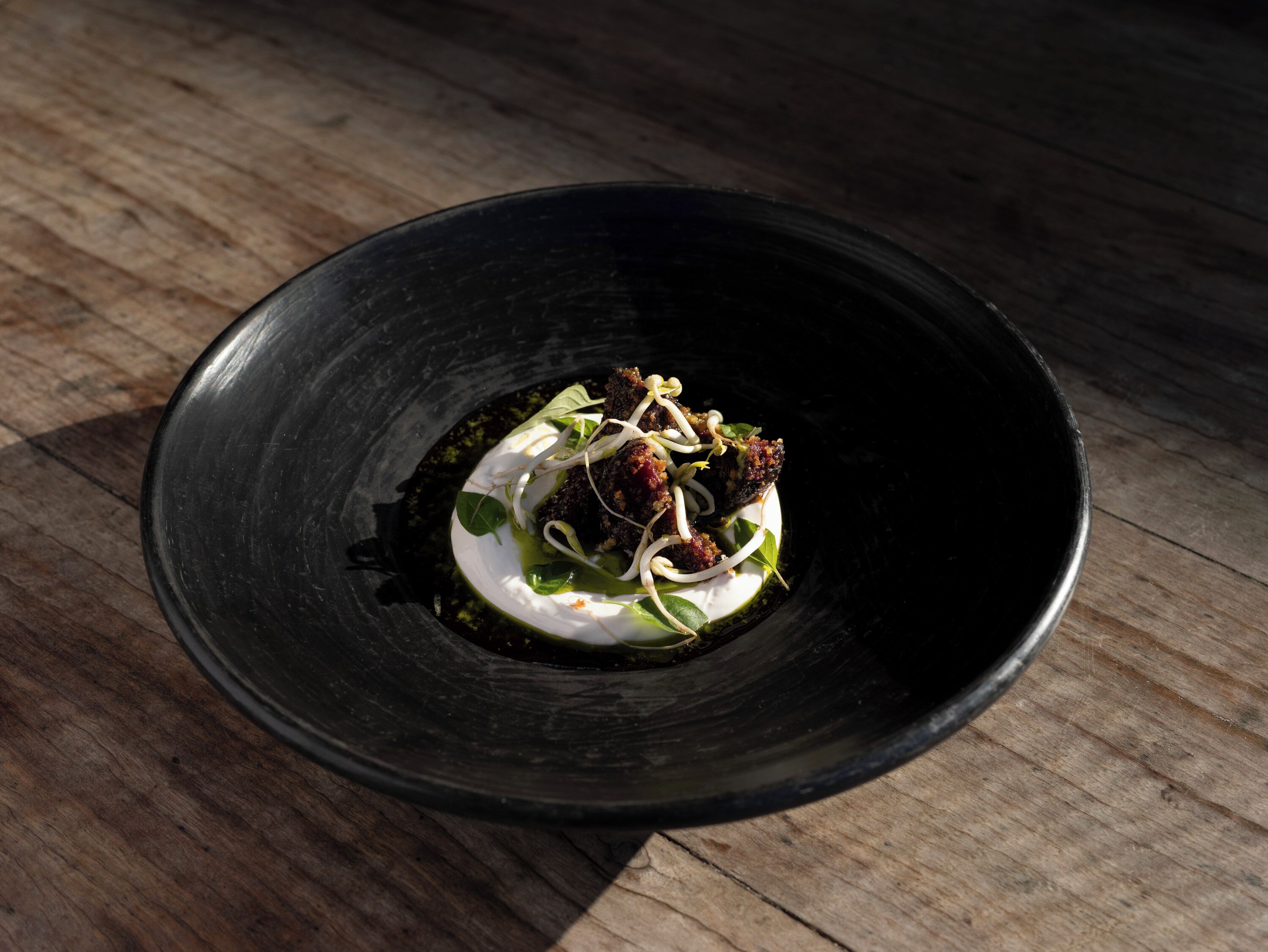 A black bowl with a dark-colored dish inside, placed on a wooden surface.