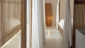 Un dormitorio con cama, mesita de noche, suelo de madera y ventana con persianas verticales.
