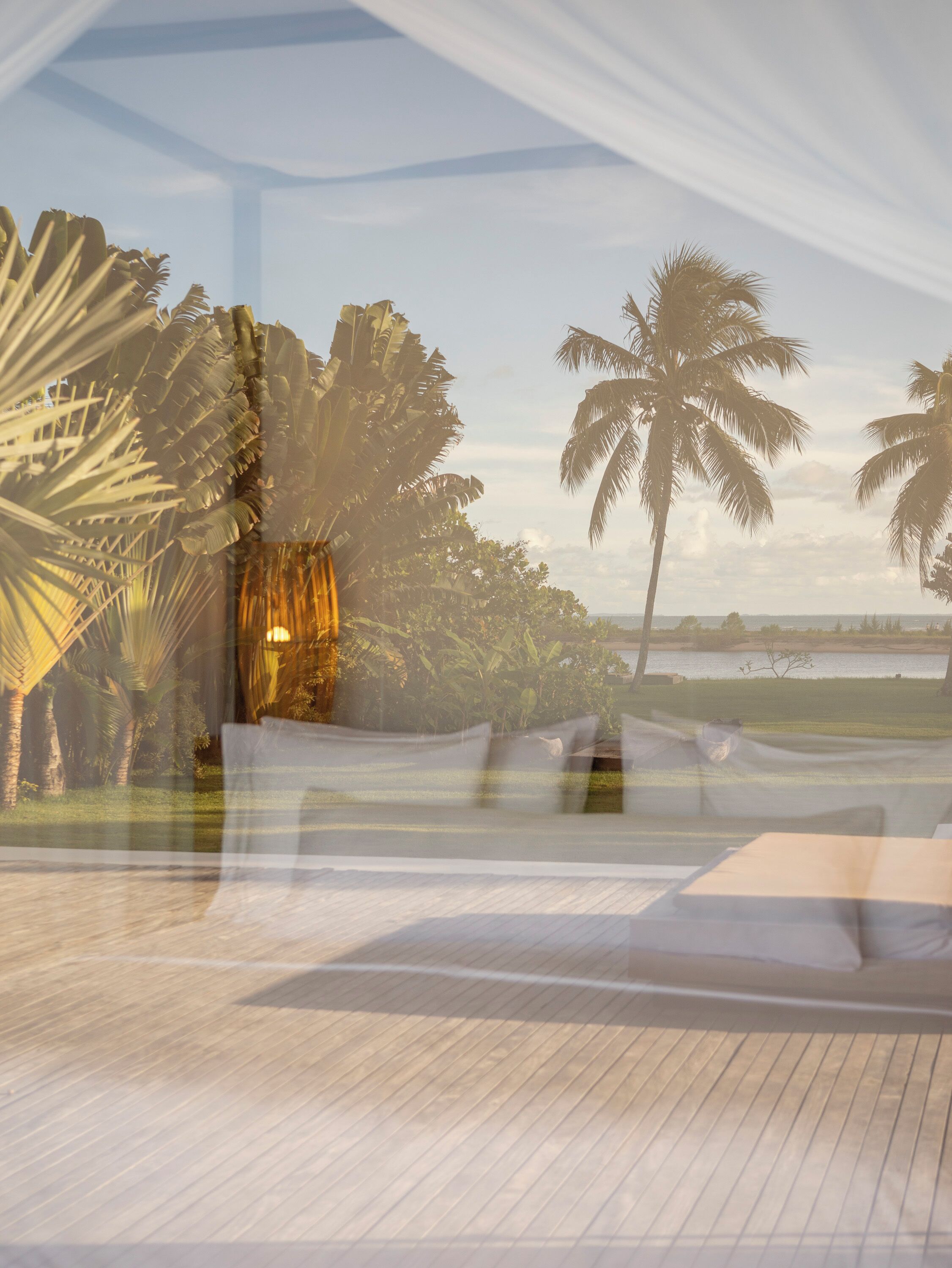 A room with a wooden floor, a bed, and a view of palm trees and a body of water.