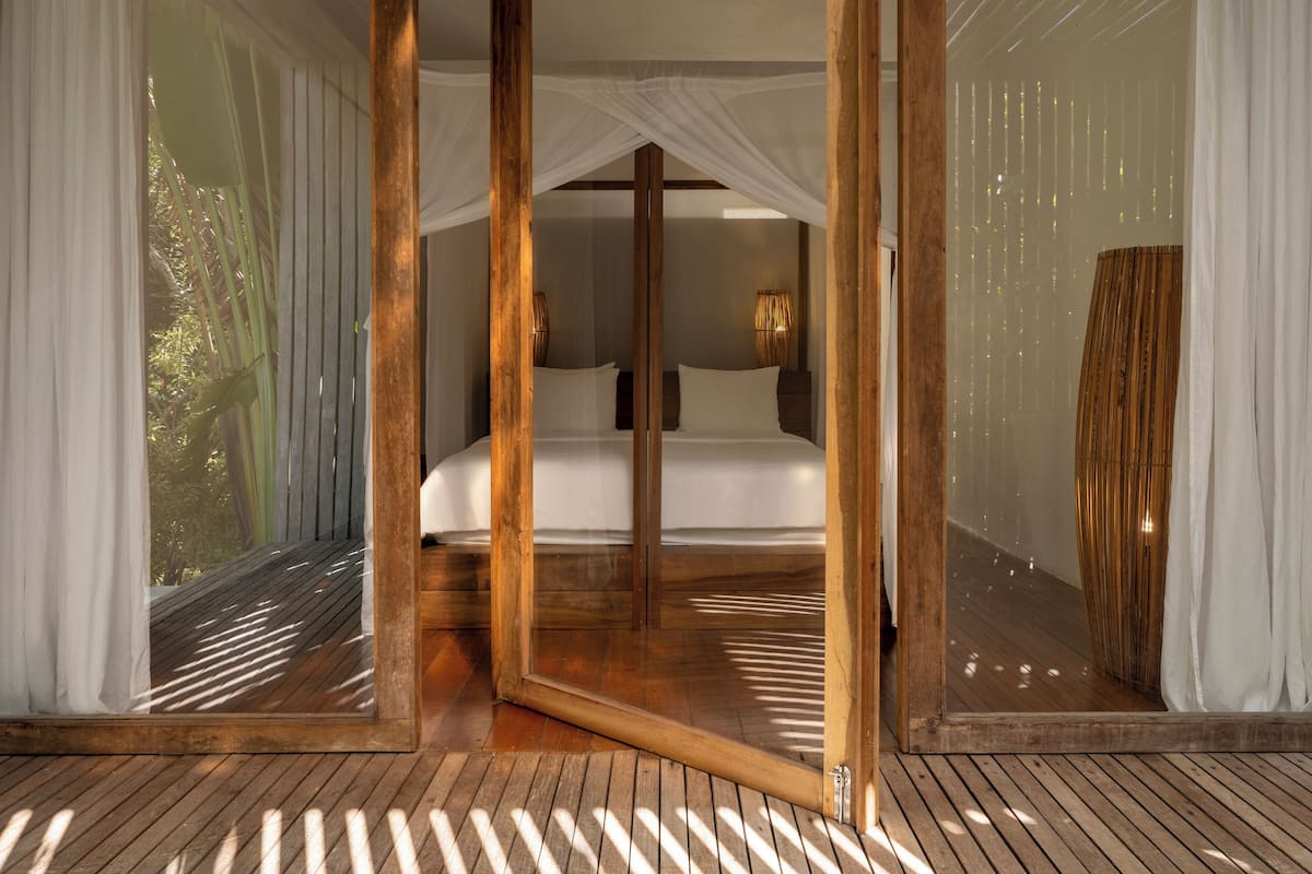Un dormitorio con piso de madera, una cama grande y cortinas translúcidas.