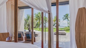 Un dormitorio con un ventanal grande, muebles de madera y vistas a un paisaje tropical.