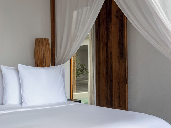 Una cama con sábanas blancas, cabecera de madera y cortinas de encaje blanco.