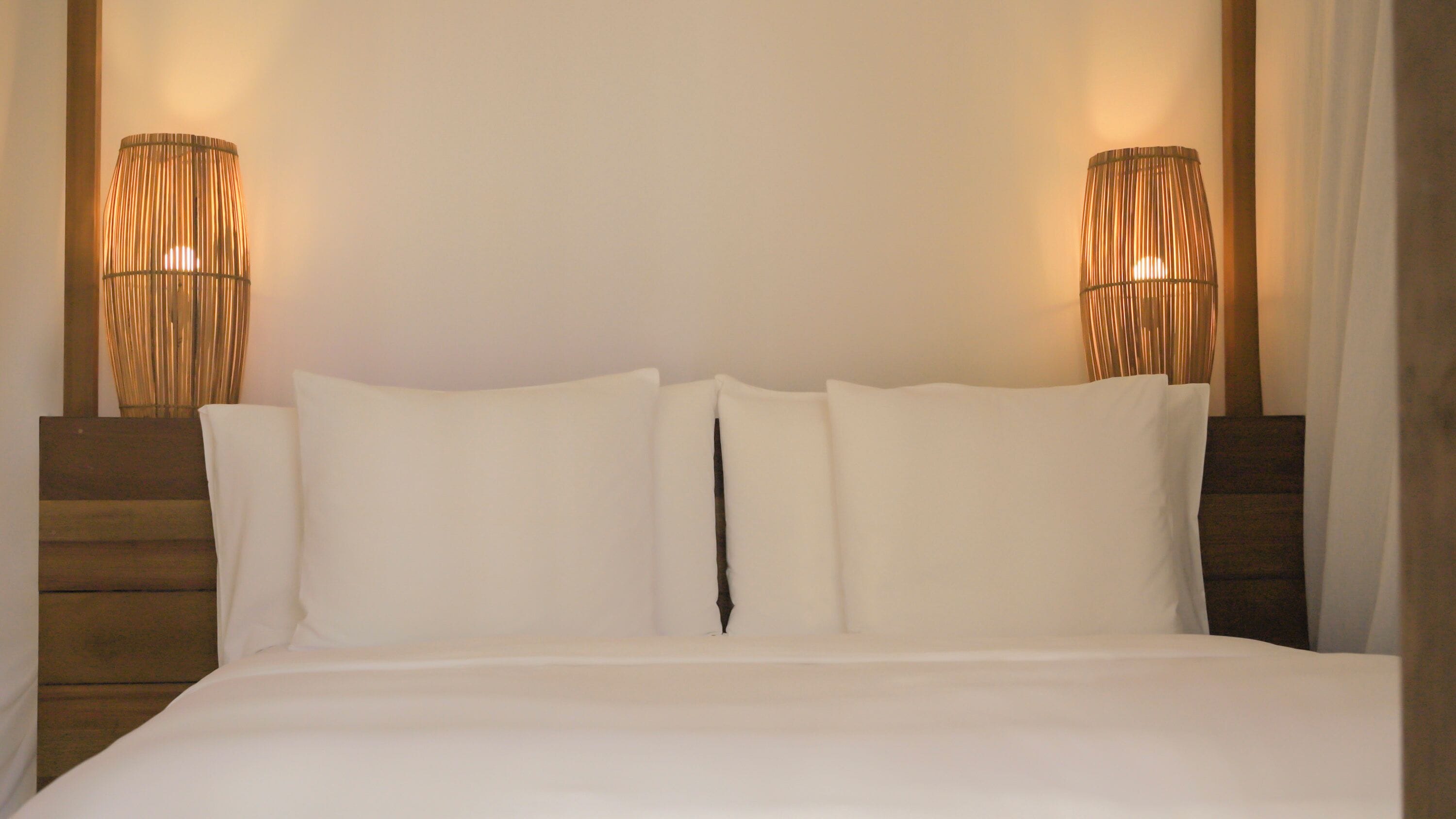 Una cama con sábanas blancas, cabecera de madera y dos lámparas fijadas a la pared.