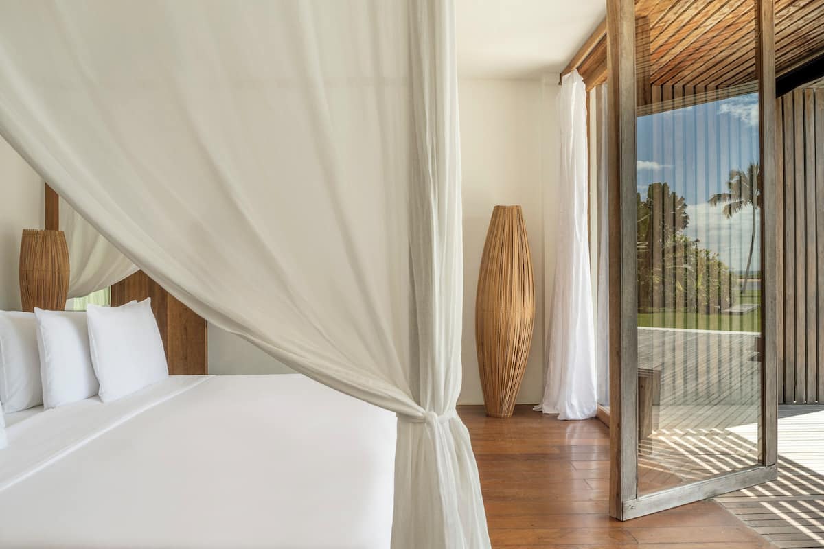 Un dormitorio con cama a dosel, suelo de madera y vistas al exterior a través de un ventanal.