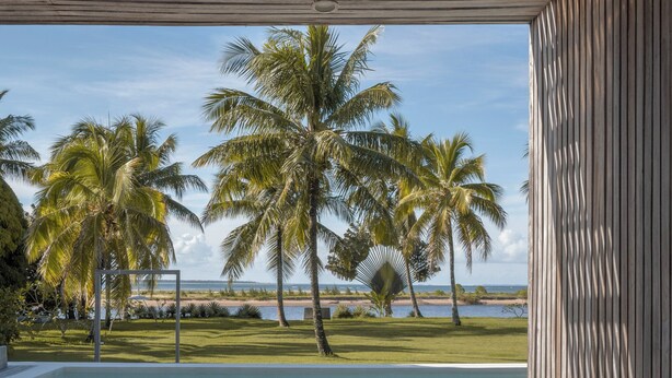 Una terraza de madera con piscina, palmeras y vista a la playa.