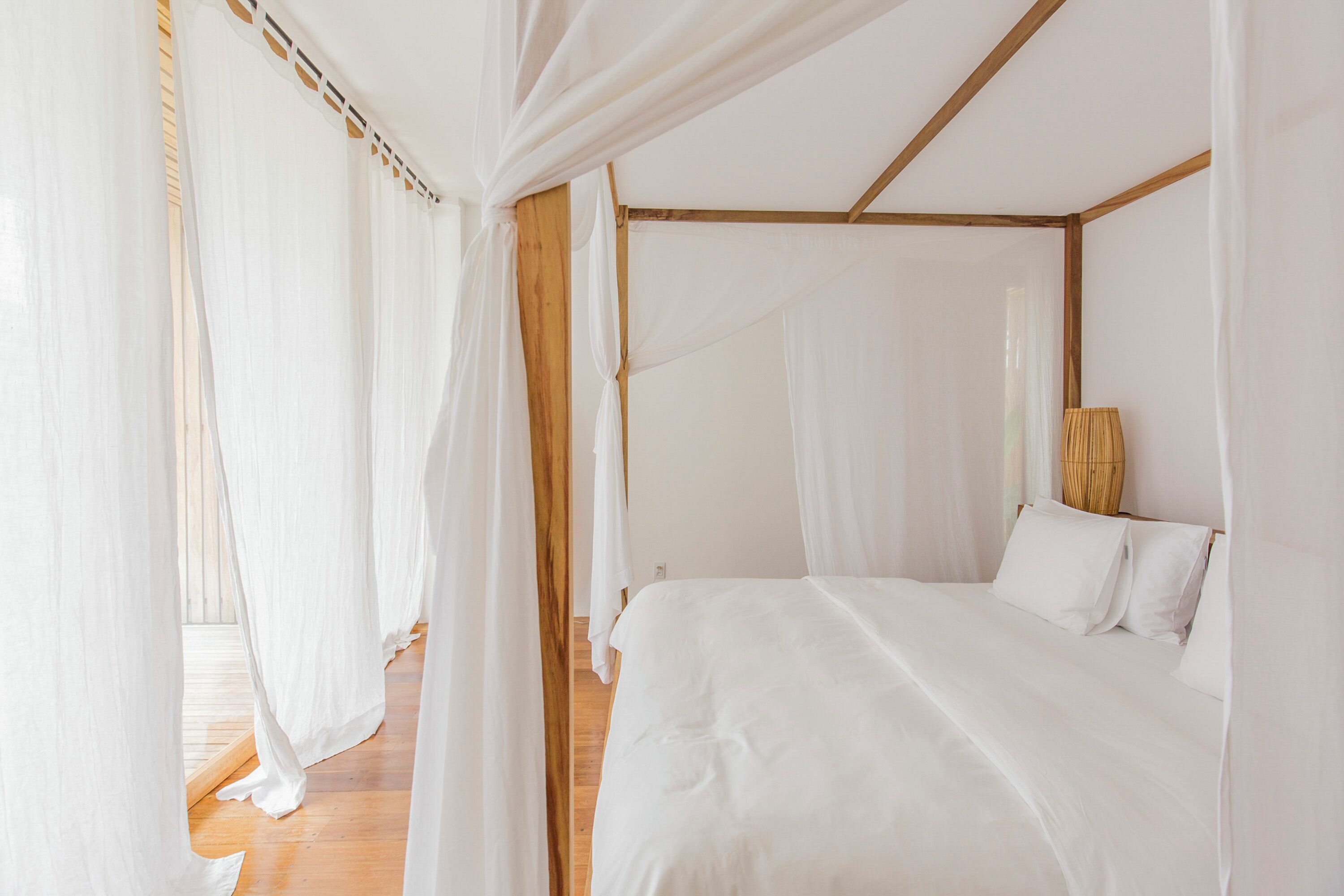 A bedroom with a four-poster bed, white bedding, and sheer curtains.