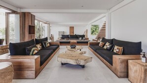 Una sala de estar moderna con un amplio sofá modular, una mesa de centro de madera y una escalera que sube a un nivel superior.