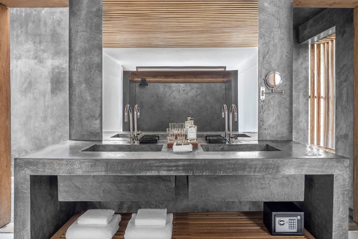 Un baño moderno con un espejo grande, dos lavamanos y un banco de madera con toallas.