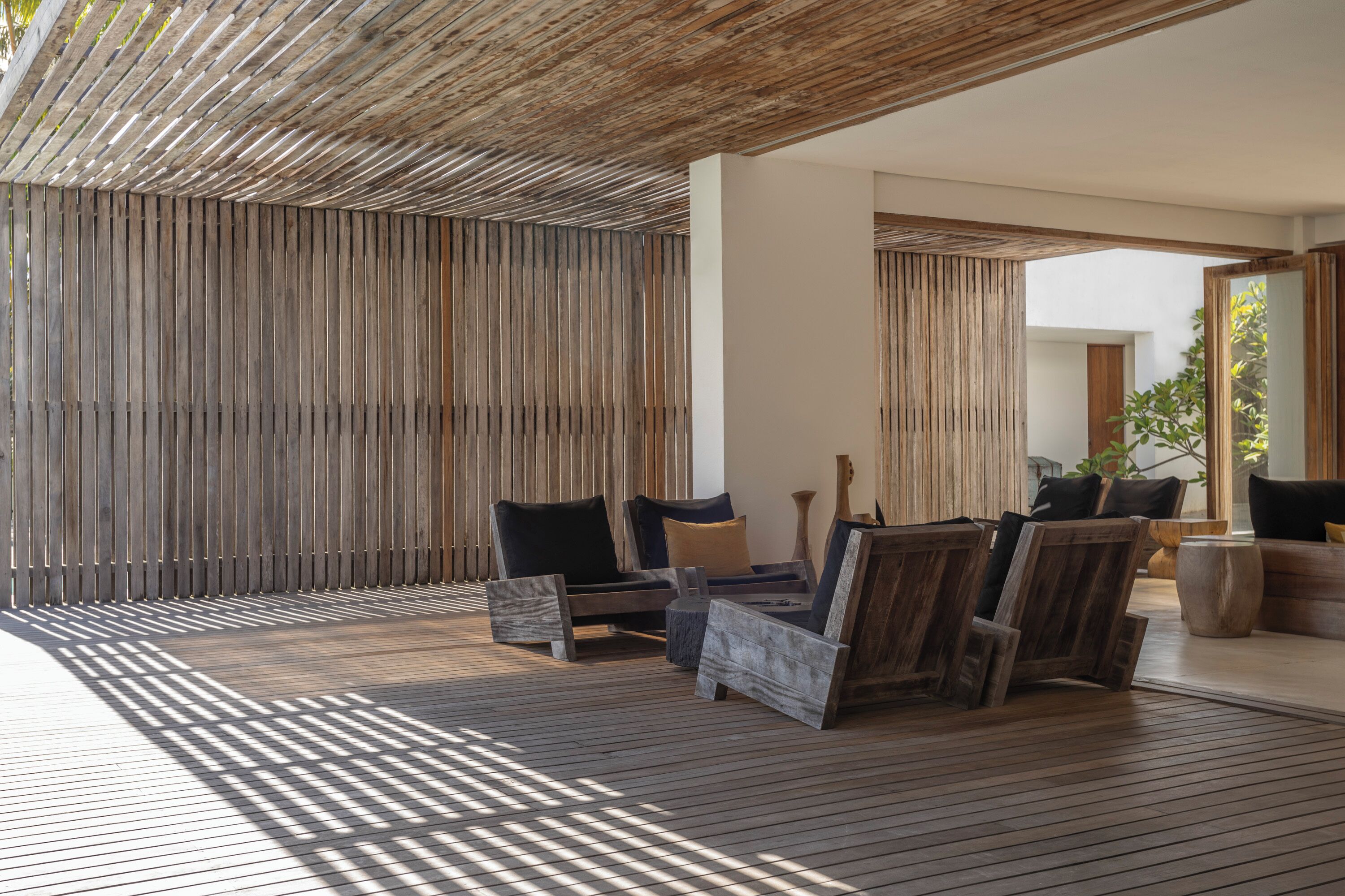 A wooden deck with outdoor furniture, including chairs and a sofa, under a wooden slatted roof structure.